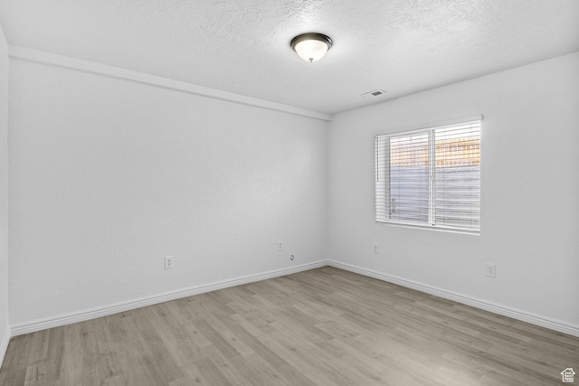 empty room featuring light wood-style floors, a textured ceiling, and baseboards