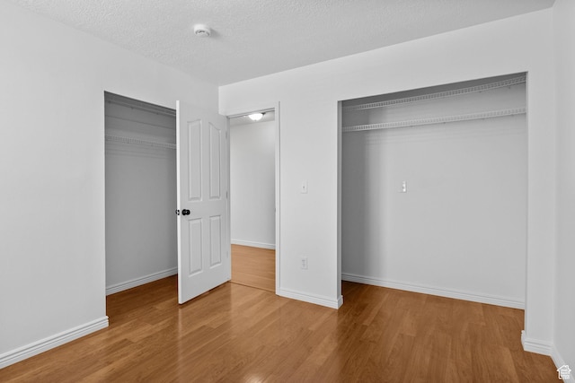 unfurnished bedroom with wood finished floors, a textured ceiling, baseboards, and multiple closets