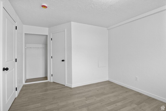 unfurnished bedroom featuring a textured ceiling, wood finished floors, baseboards, and a closet