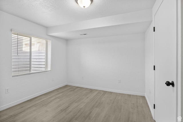 unfurnished room featuring light wood finished floors, baseboards, and a textured ceiling