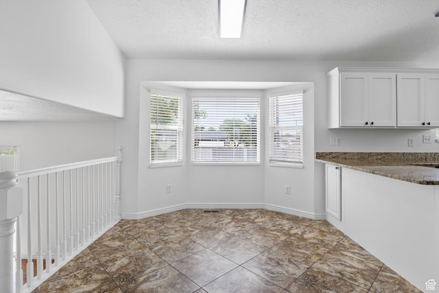 unfurnished dining area featuring a textured ceiling and baseboards