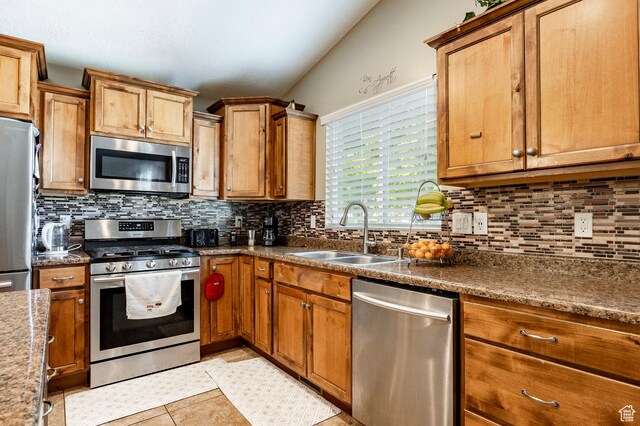 kitchen featuring stainless steel appliances, a sink, tasteful backsplash, brown cabinets, and light tile patterned flooring