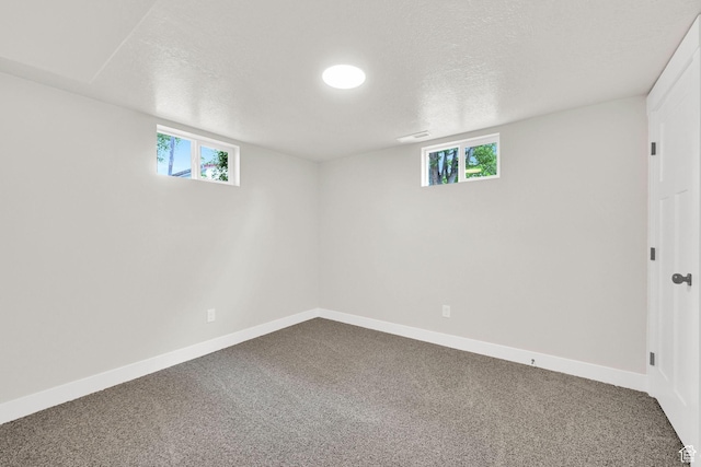 below grade area with dark colored carpet, plenty of natural light, a textured ceiling, and baseboards