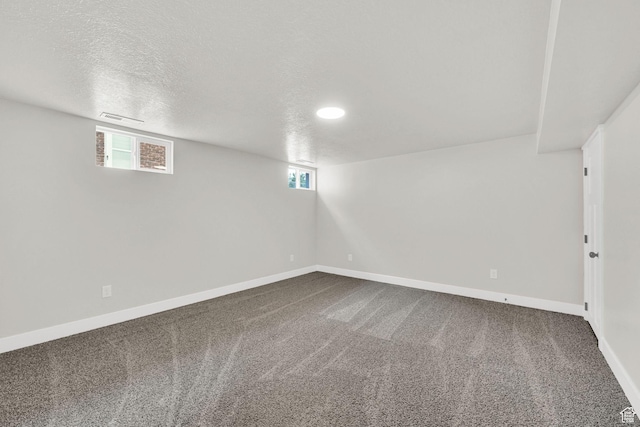 below grade area with dark colored carpet, baseboards, healthy amount of natural light, and a textured ceiling