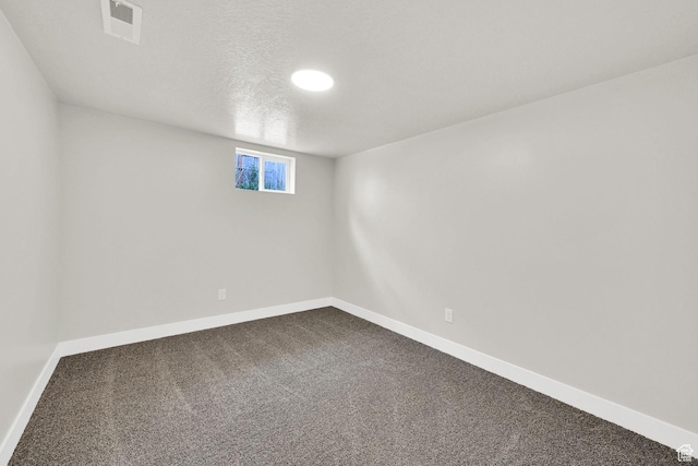basement featuring dark carpet, baseboards, and a textured ceiling