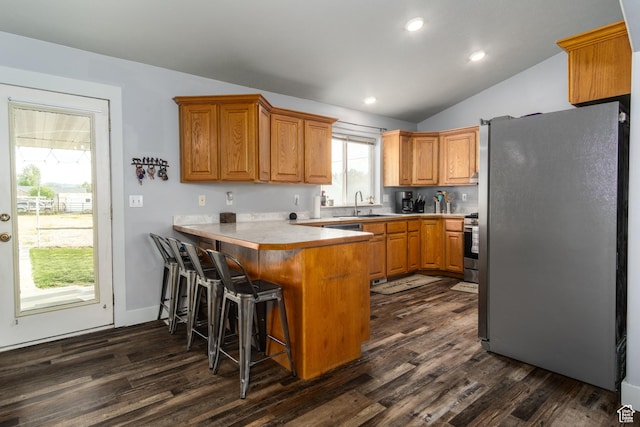 kitchen with freestanding refrigerator, a sink, a peninsula, lofted ceiling, and dark wood-style flooring