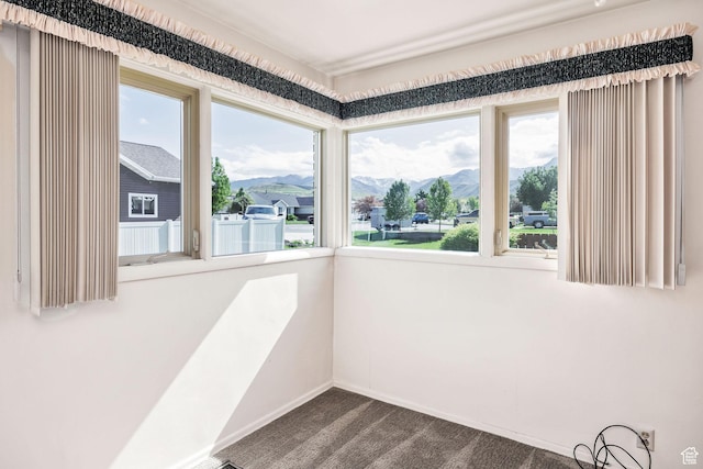 empty room featuring healthy amount of natural light, a mountain view, dark carpet, and baseboards