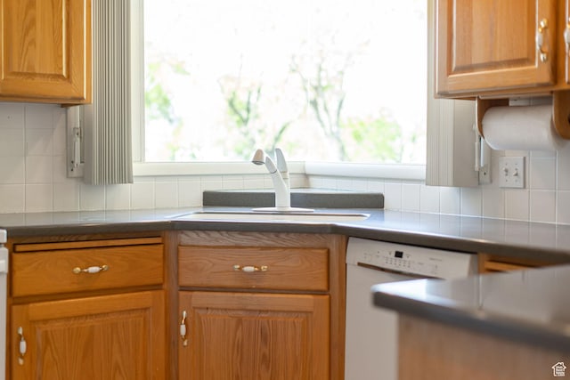 kitchen with white dishwasher, a sink, tasteful backsplash, and brown cabinets