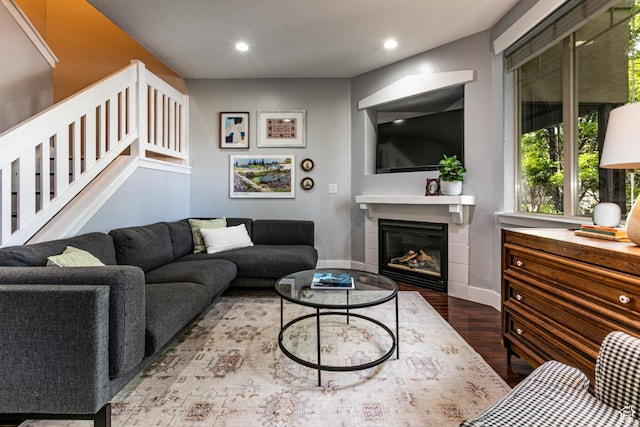 living room featuring wood finished floors, stairway, a glass covered fireplace, baseboards, and recessed lighting