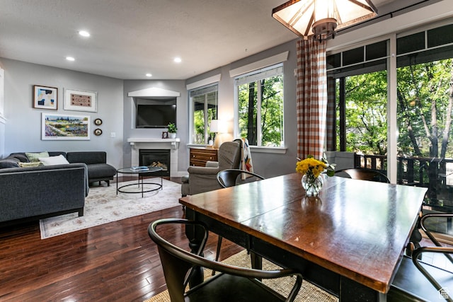 dining space with dark wood finished floors, a glass covered fireplace, recessed lighting, and a chandelier