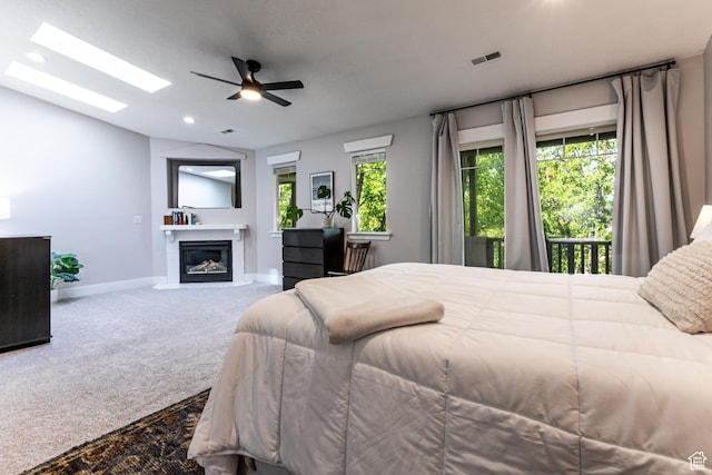 carpeted bedroom with multiple windows, baseboards, a fireplace with flush hearth, lofted ceiling, and a skylight