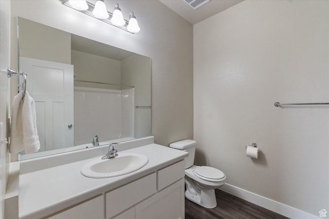 bathroom featuring wood finished floors, toilet, baseboards, vanity, and a shower