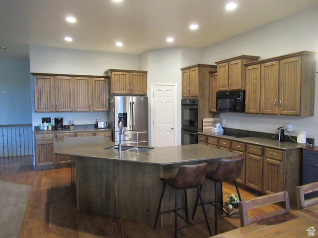 kitchen with black appliances, a kitchen island with sink, dark countertops, a kitchen bar, and a sink
