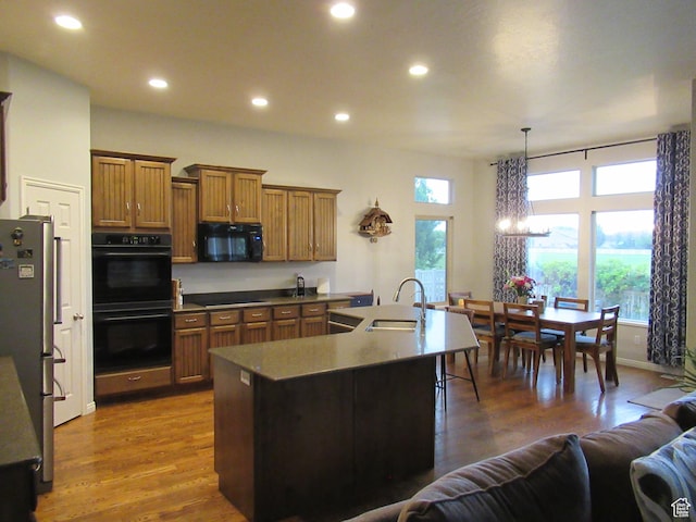 kitchen featuring black appliances, a sink, a chandelier, brown cabinetry, and dark wood finished floors