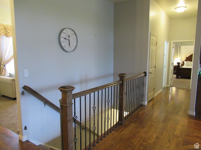 hallway with an upstairs landing, wood finished floors, and baseboards
