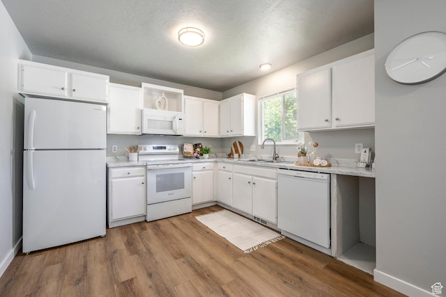 kitchen with white appliances, a sink, white cabinetry, and wood finished floors