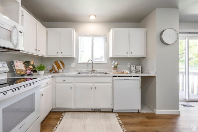 kitchen with white appliances, a sink, white cabinetry, light countertops, and light wood-style flooring