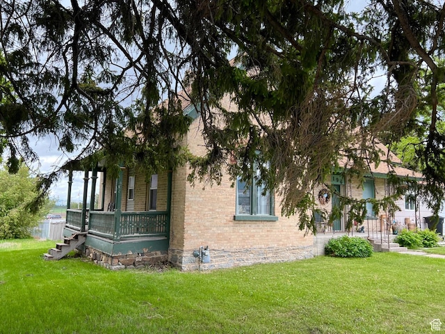 view of side of home featuring brick siding, a lawn, and a porch