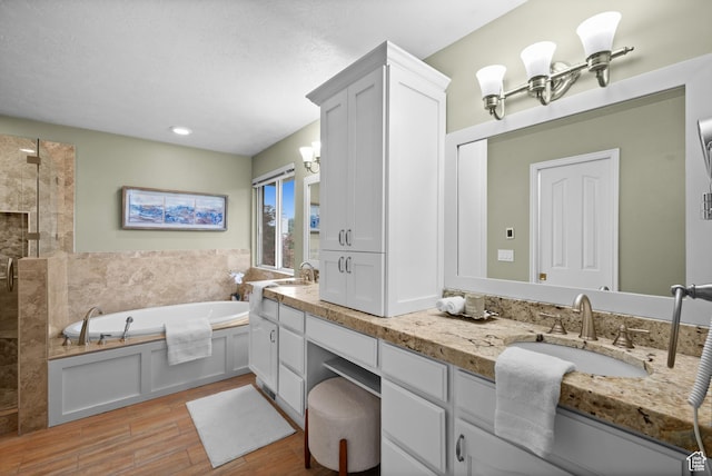 full bathroom featuring wood finished floors, a garden tub, double vanity, a tile shower, and a chandelier