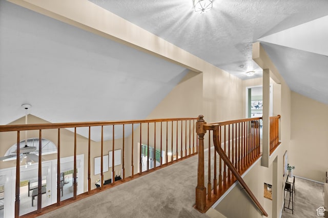 hallway featuring carpet flooring, vaulted ceiling, a textured ceiling, and an upstairs landing