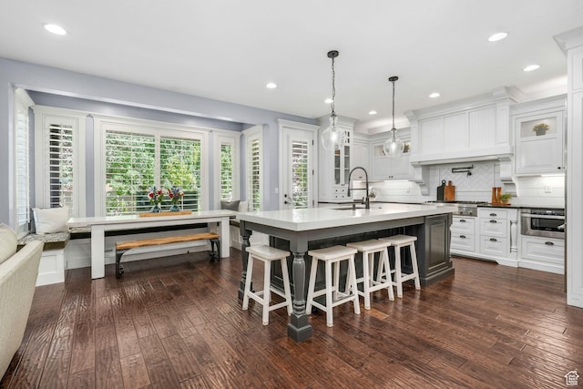 5982 N Rollins Ranch Rd W, Mountain Green, UT 84050 - kitchen with glass insert cabinets, a breakfast bar area, dark wood-type flooring, tasteful backsplash, and a center island with sink