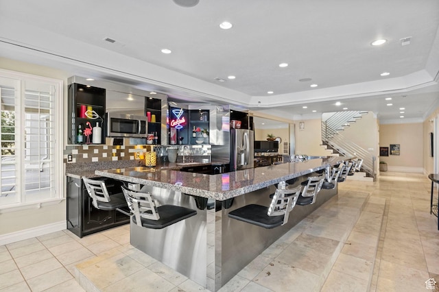 bar with a tray ceiling, recessed lighting, appliances with stainless steel finishes, baseboards, and stairway