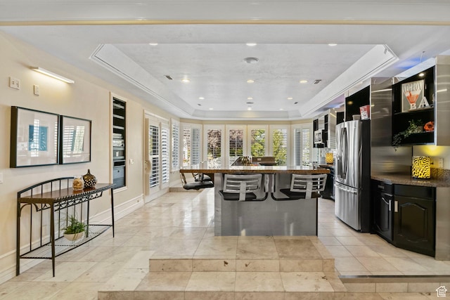 kitchen featuring stainless steel fridge, a raised ceiling, a breakfast bar, baseboards, and a kitchen island