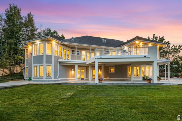 back of house at dusk with a balcony, a patio area, and stucco siding