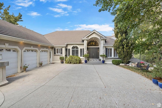 view of front of home with a tiled roof, driveway, an attached garage, and stucco siding