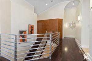 corridor with dark wood-style floors, vaulted ceiling, baseboards, crown molding, and arched walkways