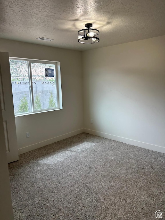 carpeted spare room with a textured ceiling, baseboards, and a chandelier