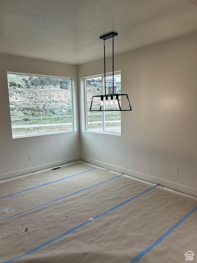 unfurnished dining area featuring a textured ceiling and baseboards
