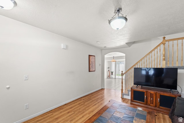 living area featuring wood finished floors, arched walkways, a textured ceiling, stairway, and baseboards