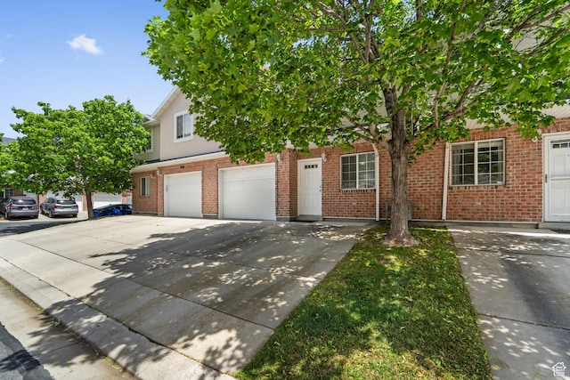 view of property hidden behind natural elements with an attached garage, driveway, and brick siding