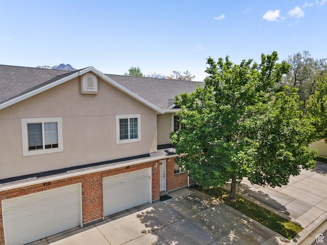 view of property with brick siding, roof with shingles, stucco siding, concrete driveway, and an attached garage