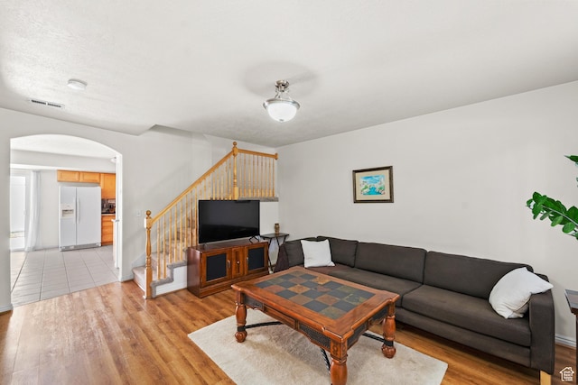 living area with arched walkways, light wood-type flooring, stairway, and baseboards