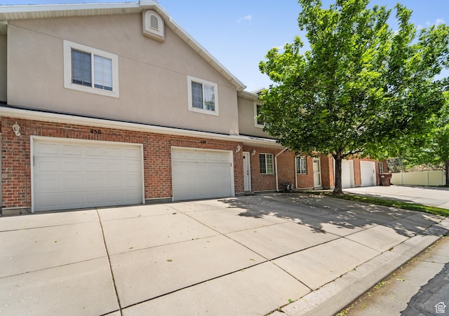 townhome / multi-family property with driveway, a garage, brick siding, and stucco siding