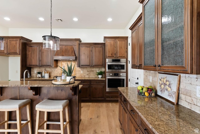 3134 S 355 W, Washington, UT 84780 - kitchen featuring a breakfast bar, custom range hood, tasteful backsplash, dark stone counters, and light wood-type flooring