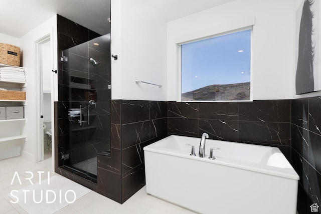 full bathroom with tile walls, a stall shower, toilet, a soaking tub, and tile patterned flooring