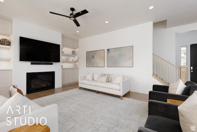living area with ceiling fan, light wood-type flooring, a glass covered fireplace, stairway, and recessed lighting