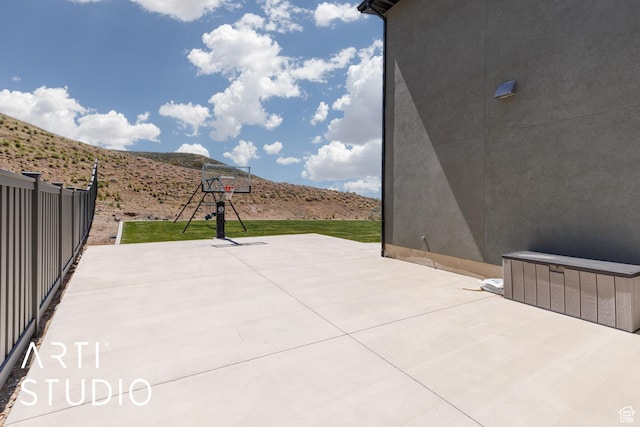 view of patio featuring fence, a mountain view, and basketball hoop