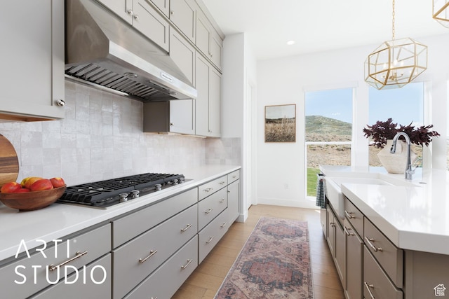 kitchen featuring under cabinet range hood, gray cabinetry, stainless steel gas cooktop, a chandelier, and backsplash