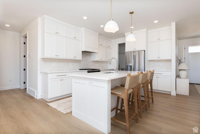 kitchen with stainless steel refrigerator with ice dispenser, a sink, backsplash, light wood-type flooring, and recessed lighting