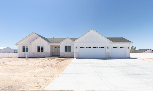 modern farmhouse featuring a garage, board and batten siding, concrete driveway, fence, and stone siding
