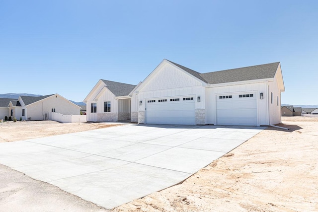modern farmhouse with a garage, board and batten siding, driveway, and stone siding