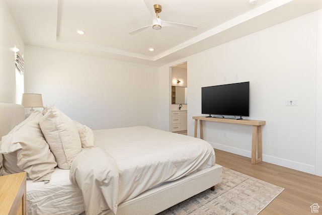 bedroom with light wood finished floors, baseboards, a tray ceiling, recessed lighting, and ensuite bath