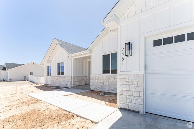 view of side of property with board and batten siding, stone siding, fence, and a garage