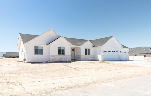modern farmhouse with an attached garage, board and batten siding, concrete driveway, stone siding, and fence