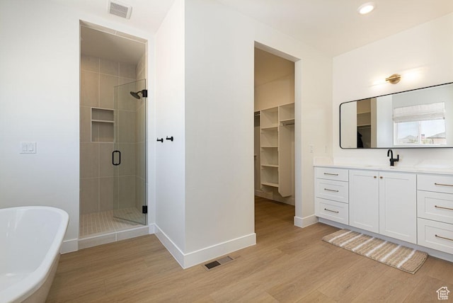 bathroom with a shower stall, wood finished floors, vanity, a freestanding tub, and baseboards