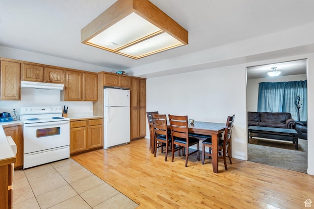 kitchen with white appliances, under cabinet range hood, light countertops, light wood-style flooring, and brown cabinets